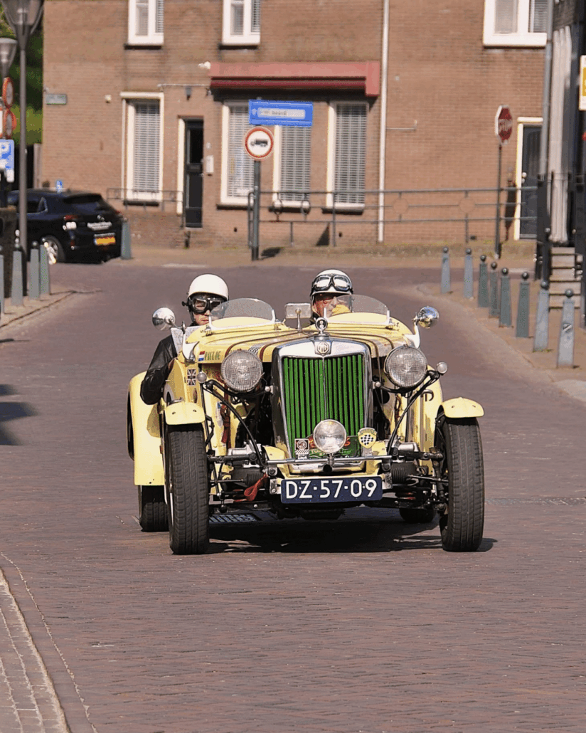 je ziet 2 mannen in een oude auto zitten in een straat