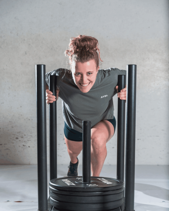 gewichtensled-sportschool-website Vrouw glimlacht terwijl ze een gewichtensled duwt in de sportschool