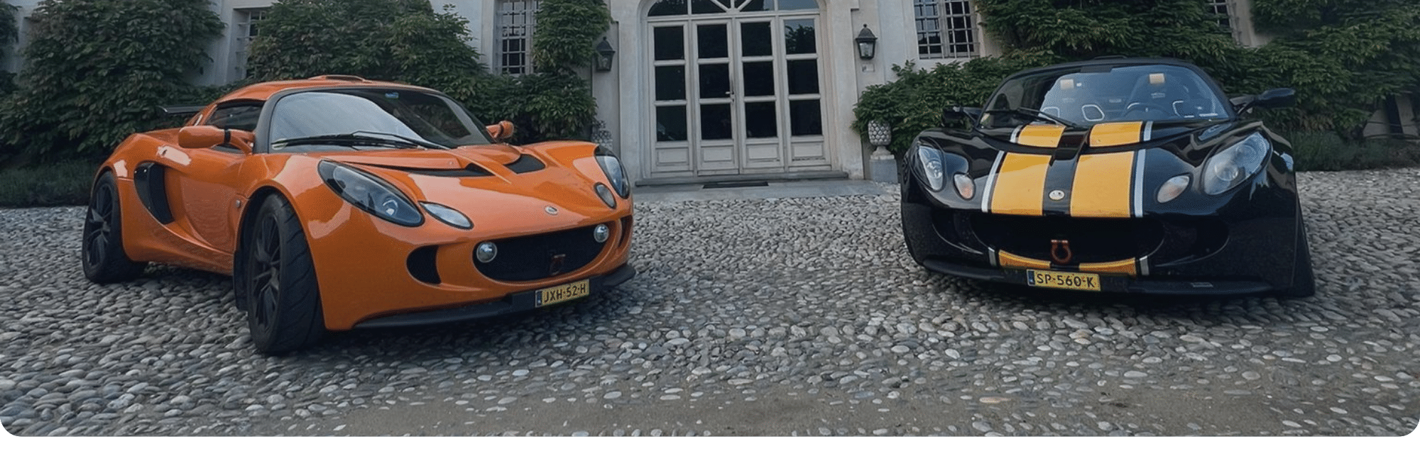 oranje-sportwagen-weemaes-technic Oranje sportwagen naast een zwarte auto voor een wit gebouw